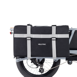 Black Velotric Packer Pannier Bag secured with adjustable straps on bike rack.