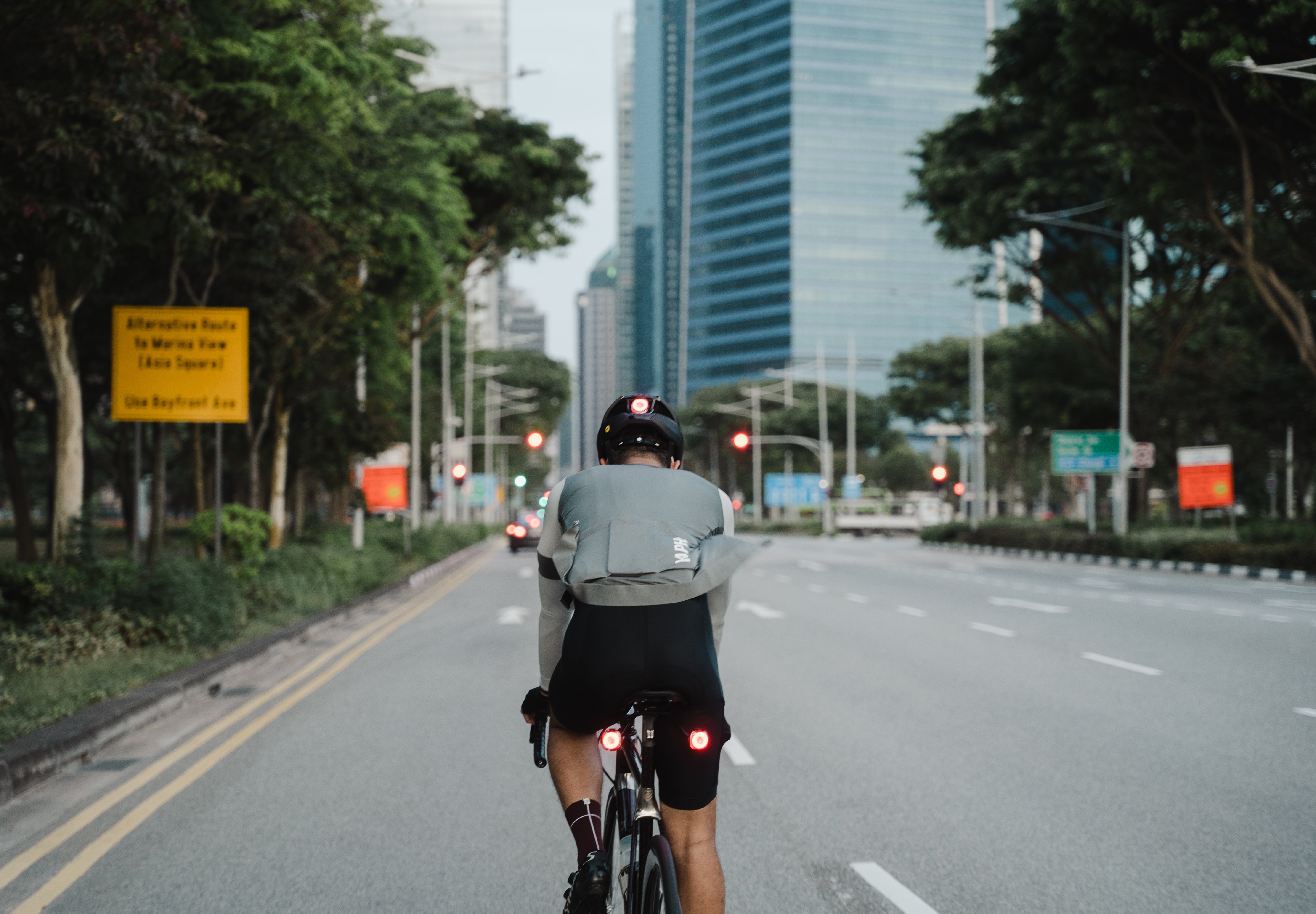 Cyclist in Lumos Ultra Fly Pro helmet riding on urban road with traffic signs.