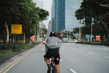 Cyclist in Lumos Ultra Fly Pro helmet riding on urban road with traffic signs.